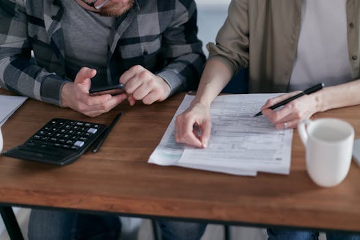 A couple diligently reviews their finances using a calculator and documents at home.