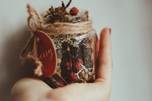A hand holding a festive rustic jar with dried herbs and spices, adorned with a 'merry' tag.