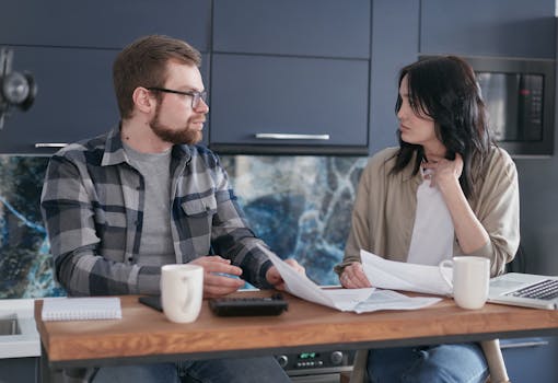 A young couple sitting at a table discussing bills and financial plans in a modern kitchen.