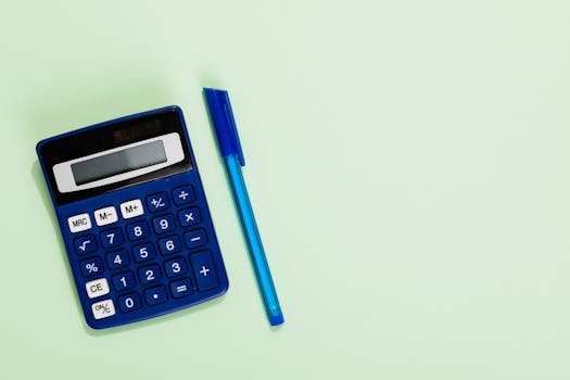 Blue calculator and pen on a pastel green background with ample copy space. Ideal for education and finance themes.