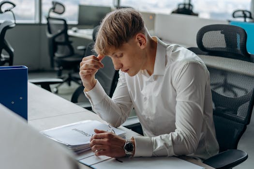 Man in white shirt focused on reading documents at a modern office desk.