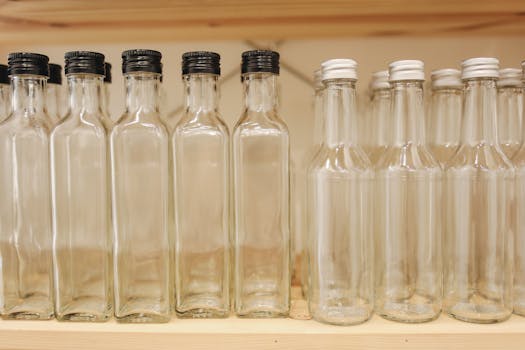 Multiple clear glass bottles with caps on a wooden shelf, promoting zero waste.