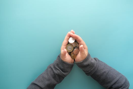 Two hands holding a stack of coins against a blue background, symbolizing savings or financial security.