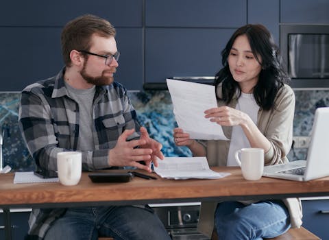 Young couple managing their finances with laptop and documents in a modern kitchen setting.